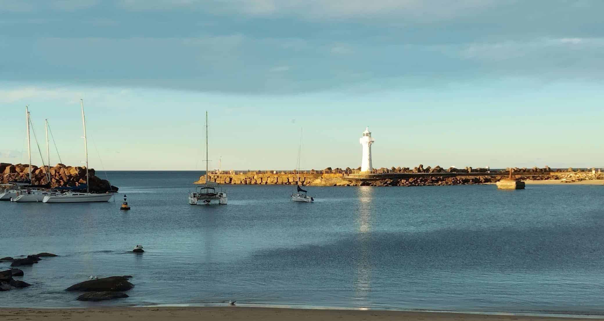 Wollongong Coastal harbor scene with sailboats, lighthouse, and breakwater.